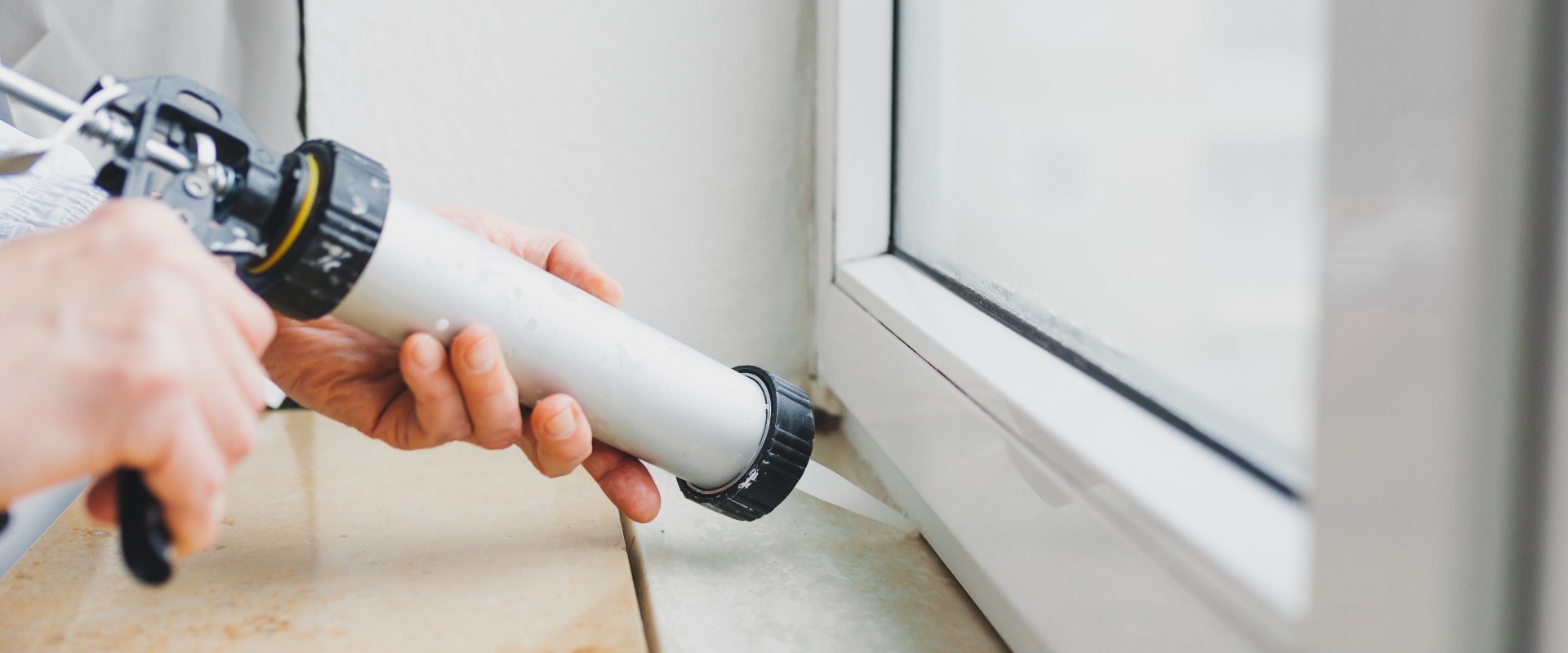 Hands of worker using a silicone tube for repairing of window